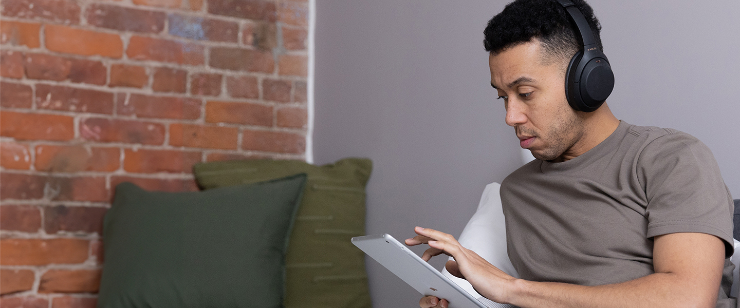 A man sat down on a sofa holding a tablet device smiling