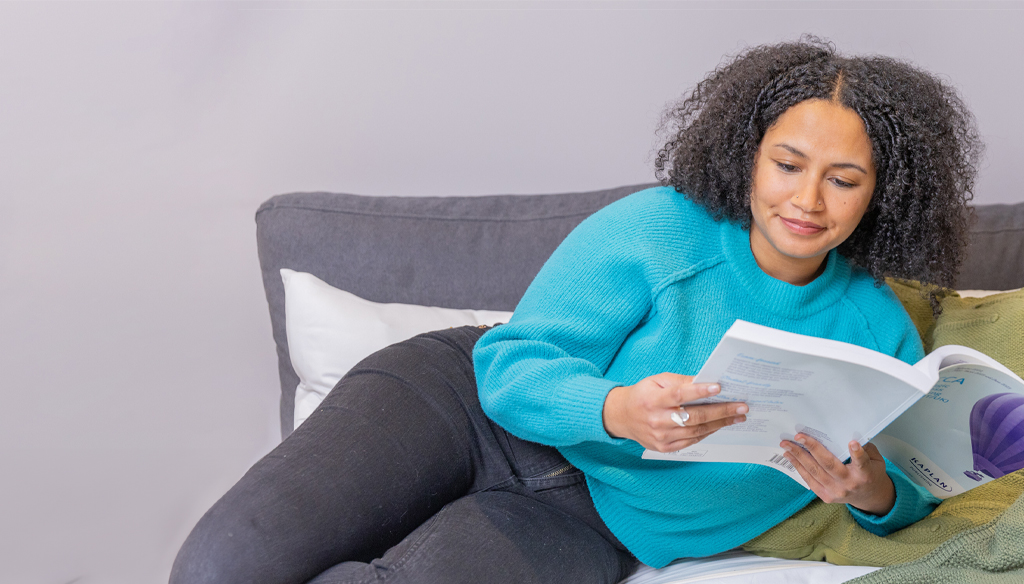 Woman lying on a sofa reading a Kaplan textbook