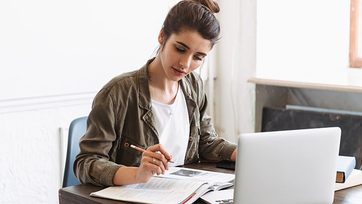 woman looking at book in front of laptop