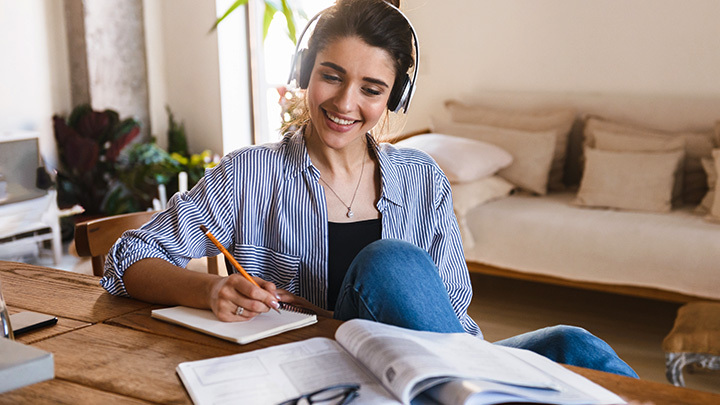 Woman at home, writing on notepad, with headphones on